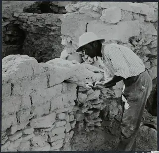 Man in a pith helmet sawing a mud-brick wall at Idalion during excavation