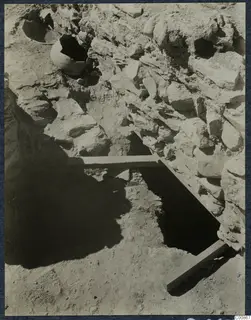 Excavation trench at Idalion Acropolis with a rough stone wall, broken pottery vessels in the soil and wooden boards laid across the cut