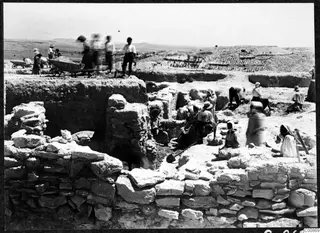 Excavation at F7, Idalion, with workers digging among exposed stone walls beside a wheelbarrow.