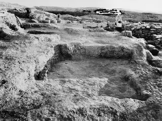 Rectangular excavated pit at Idalion with a stone wall and a seated person beyond it