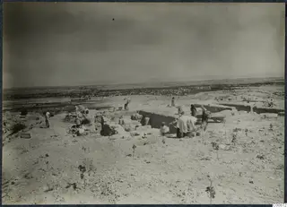 Workers excavating walls on the acropolis at Idalion, with a wide plain and town below.