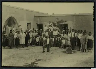 Farewell party: a large group of people posed in a dusty courtyard in front of a whitewashed building at Idalion.