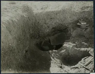 Excavation trench at Idalion Acropolis with a broken pottery vessel lying in a pit and a stack of flat stones