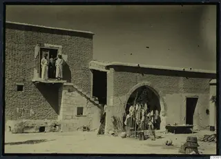 Mud-brick house at Idalion with three men on a balcony and an arched doorway hung with cloth