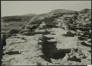 Excavated wall foundations on the Idalion acropolis, with a trench in the foreground and hills behind.