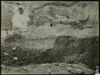 Excavation at Plakes, Lapithos, with two people among trench walls and a wooden box.