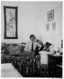 Vivi Gjerstad seated on a floral-covered sofa in a room with wall hangings and framed pictures, Nicosia