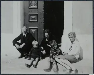 Five people, two adults and three children, sitting on a stone step in front of a dark wooden door.