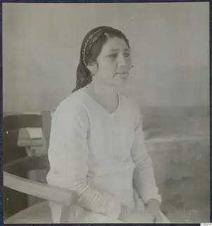 Portrait of Maria in Nicosia, a woman in a headscarf and light blouse seated in a wooden chair.