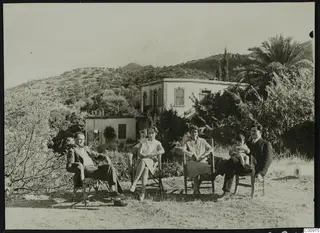 Erik Sjoqvist, Rosa Lindros and others seated outdoors in front of a white house on a hillside.