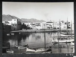 Kyrenia harbour with whitewashed buildings along the quay, moored boats on the water and mountains behind.