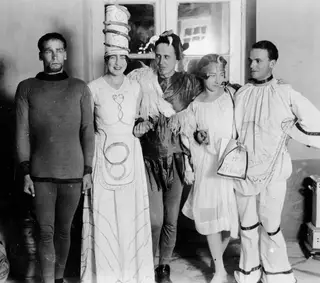 Five people in costumes posing together for a masquerade in a room with a doorway behind them.