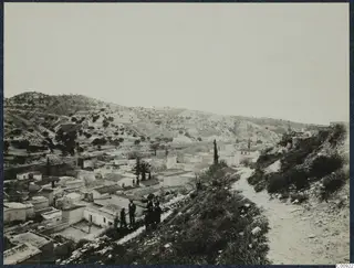 Kalavasos village seen from a slope, with flat-roofed houses, scrubby hills behind and a small group of people standing nearby.