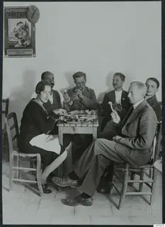 Six people eating and drinking around a small table in a whitewashed room in Lapithos