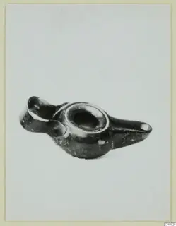 Black-glazed lamp with a central filling hole, a broken nozzle at left and a long handle at right, on a pale background.