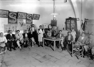 Men seated and standing in the Christoforos café at Lapithos, with a waiter holding a tray of cups.