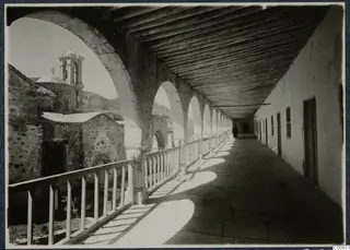 Covered arcaded gallery with a timber roof and a single man walking far along it, monastery buildings at Lambousa