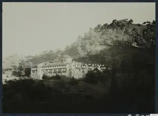 Machairas monastery, a long whitish multi-storey building with a small tower on a wooded hillside, seen from the west
