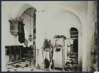 Interior of the monastery church, Lambousa, with a carved wooden pulpit and a tall stand draped with white cloth.
