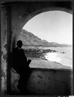 John Lindros seated in an arched opening of a plastered wall, looking out over the coast at Lambousa monastery.