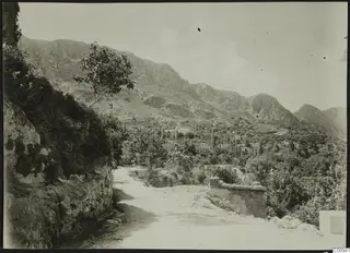 Landscape view from the school at Lapithos, with a dirt road, rocky hillsides and village houses among trees.