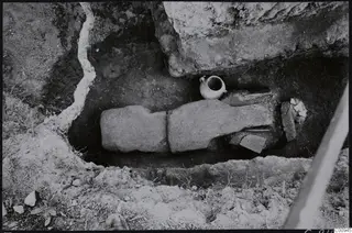 Excavated cut at Lapithos Tomb 422 with two long stone slabs laid over the fill and a small jug beside them.
