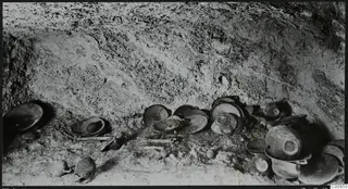 Tomb 428 at Lapithos: pottery vessels and pale bones lying on the floor of a tomb chamber during excavation