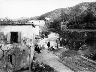 Village street at Kylistra, Lapithos, with whitewashed houses, several people and an excavated earth bank at right