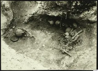 Kylistra tomb at Lapithos during excavation, with pottery vessels in the niche and a skeleton beside them