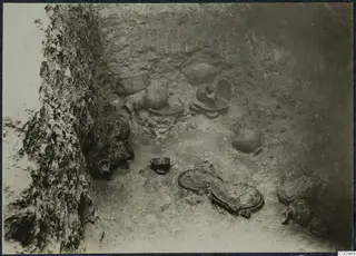 Pottery vessels lying in situ on the floor of an excavated pit, with a rock-cut wall on the left.
