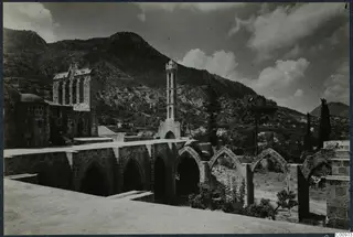 Monastery at Bellapais: stone buildings with arched arcades, a tower topped by a cross, and a steep hill behind.