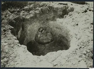 Excavation cut at Idalion with a rounded mass of stones and earth in its centre, surrounded by loose stones and pale soil.