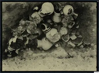 Pottery vessels and sherds lying in situ in a dark excavated hollow at Idalion Acropolis.