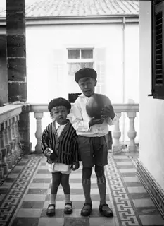 Two boys in berets stand on a tiled veranda in Nicosia, one holding a large ball.