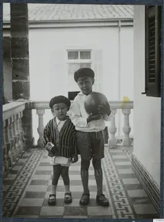 Two young boys standing on a tiled veranda, one holding a large ball, in Nicosia