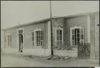 A single-storey rendered building with shuttered windows and a man standing in the doorway, Nicosia