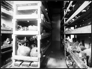 Storeroom shelves in Nicosia holding many pottery vessels, jugs and jars on wooden racks.