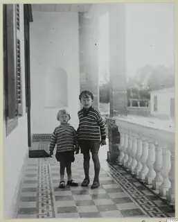 Two young boys standing on a tiled veranda beside a white balustrade in Nicosia.