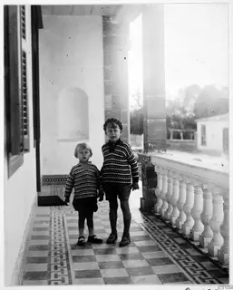 Two boys in knitted jumpers stand on a tiled veranda in Nicosia, facing the camera.
