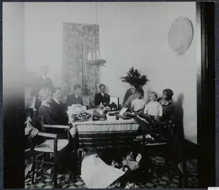 Christmas Eve 1928 gathering around a table of presents, with about ten people and two children in a room