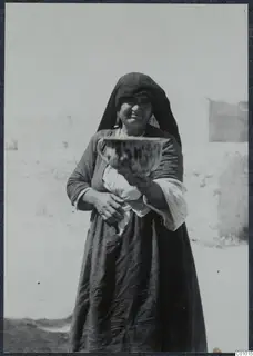 Smiling woman in a dark headscarf and dress holding a large bowl with dark streaked glaze, Karpas peninsula