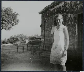 Gudrun Atterman standing outside a stone house at Vouni, with a tree and open ground behind her.