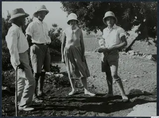 Four people in pith helmets and light clothing standing on dry ground at Vouni, one holding a small pale object.