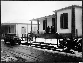 The Swedish house in Nicosia: a white house with a columned veranda, people on the steps and a dark car in the snowy street.