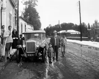 Group of people beside an early car on a muddy, snowy street in Nicosia, with a child in a beret in front