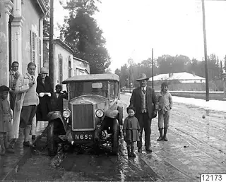 Street in Nicosia with an old car and a group of adults and children standing beside it, patches of snow on the ground