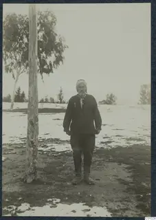 Man in a striped turban and dark jacket standing on patchy snow beside a tall bare tree trunk, Nicosia