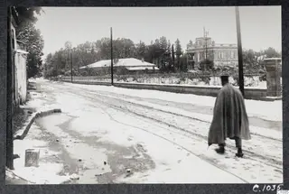 Snow-covered Gladstone Road in Nicosia, with a man in a long cape walking away along the street