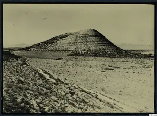 Steep conical hill rising from open dry land at Idalion, with terraced slopes and a dirt track below.