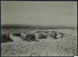 Ruined stone walls on a stony hilltop at Idalion, with a town and hills in the distance